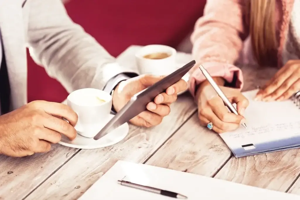 Two people sitting at a table with coffee and cell phones.