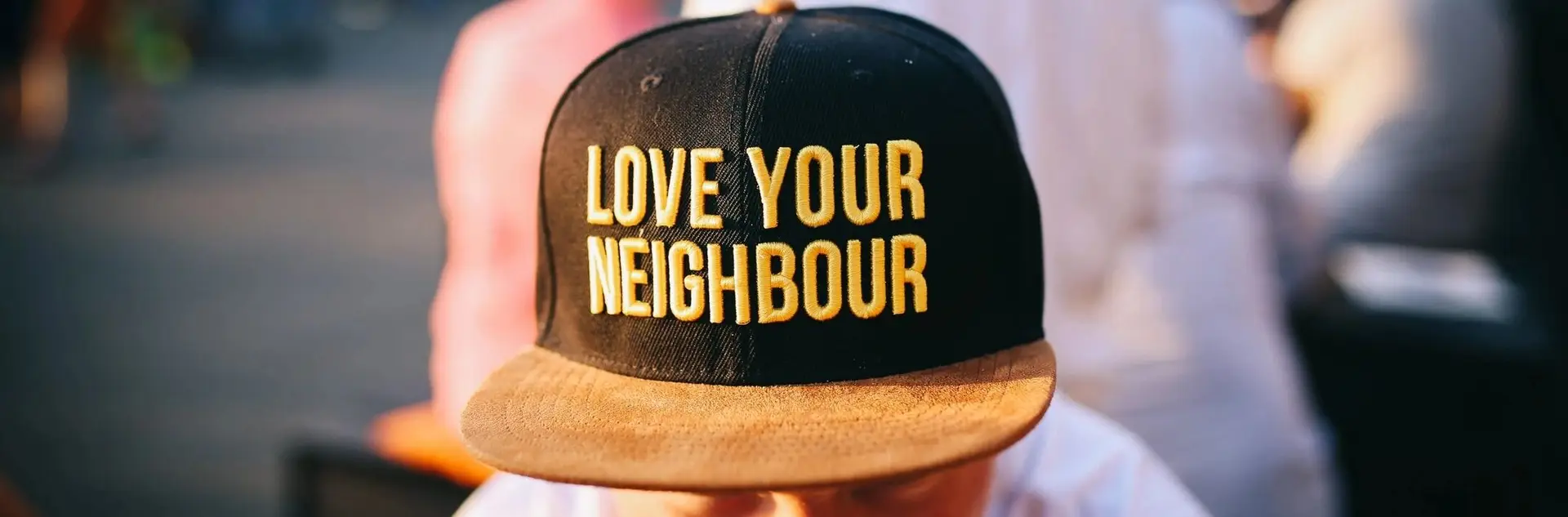 A black and brown hat with the words " love your neighbour ".